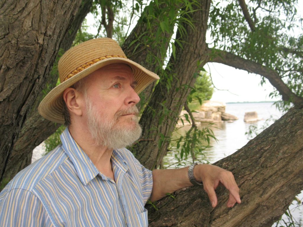 Photo of Artist, Richard Gold, resting his arm on a tree limb in a nature scene.